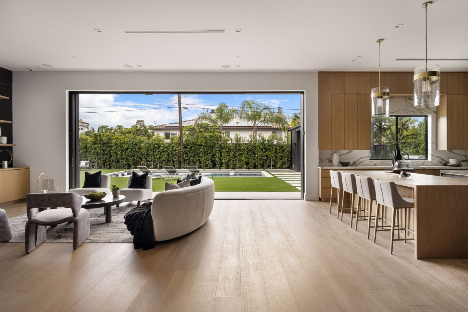 Modern open-plan living room and kitchen with large glass doors leading to a well-manicured backyard.